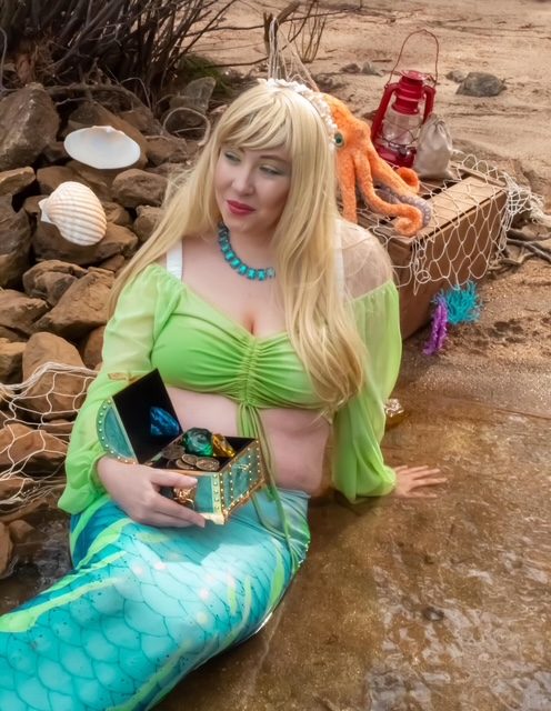 Blonde mermaid on a sandy shore holding a treasure box